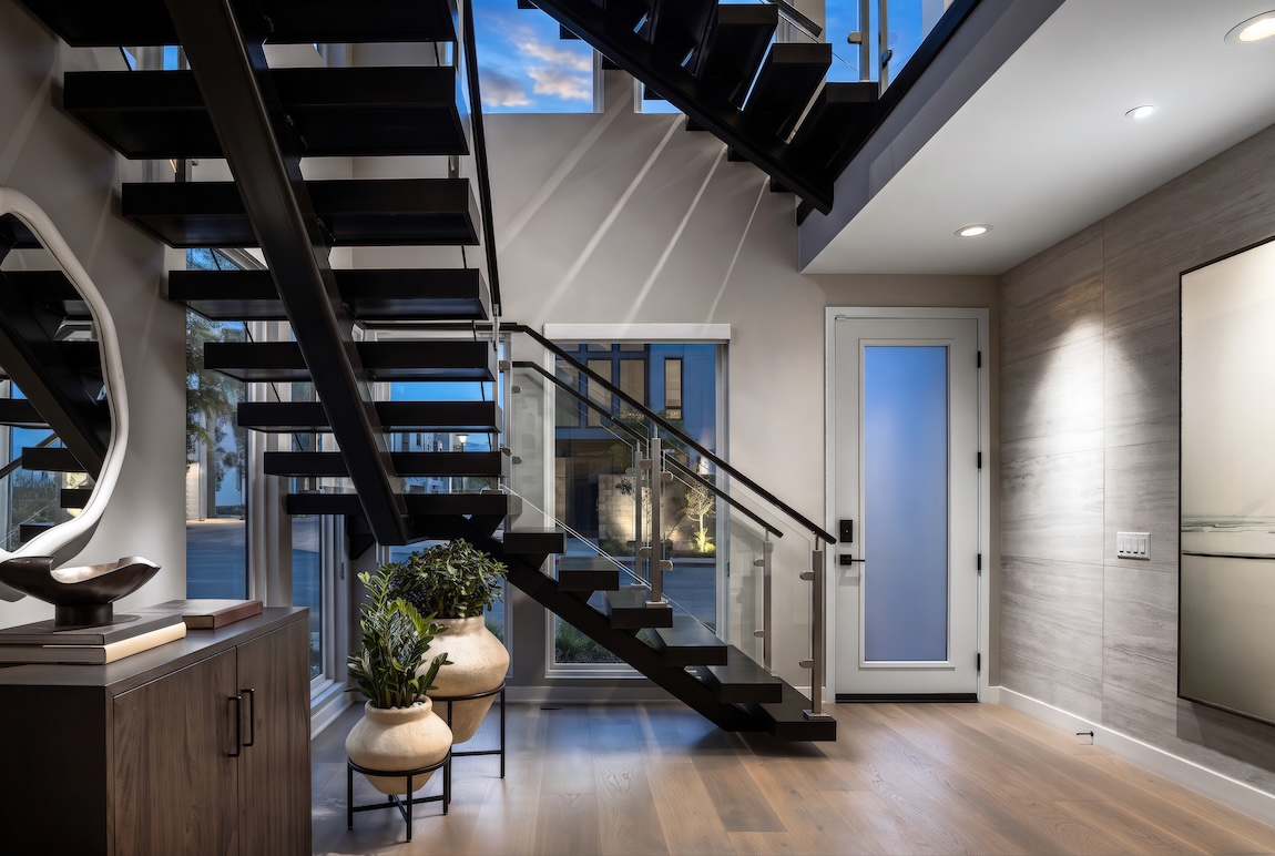 Modern entryway featuring a floating staircase with black open risers, glass railings, and wood flooring.