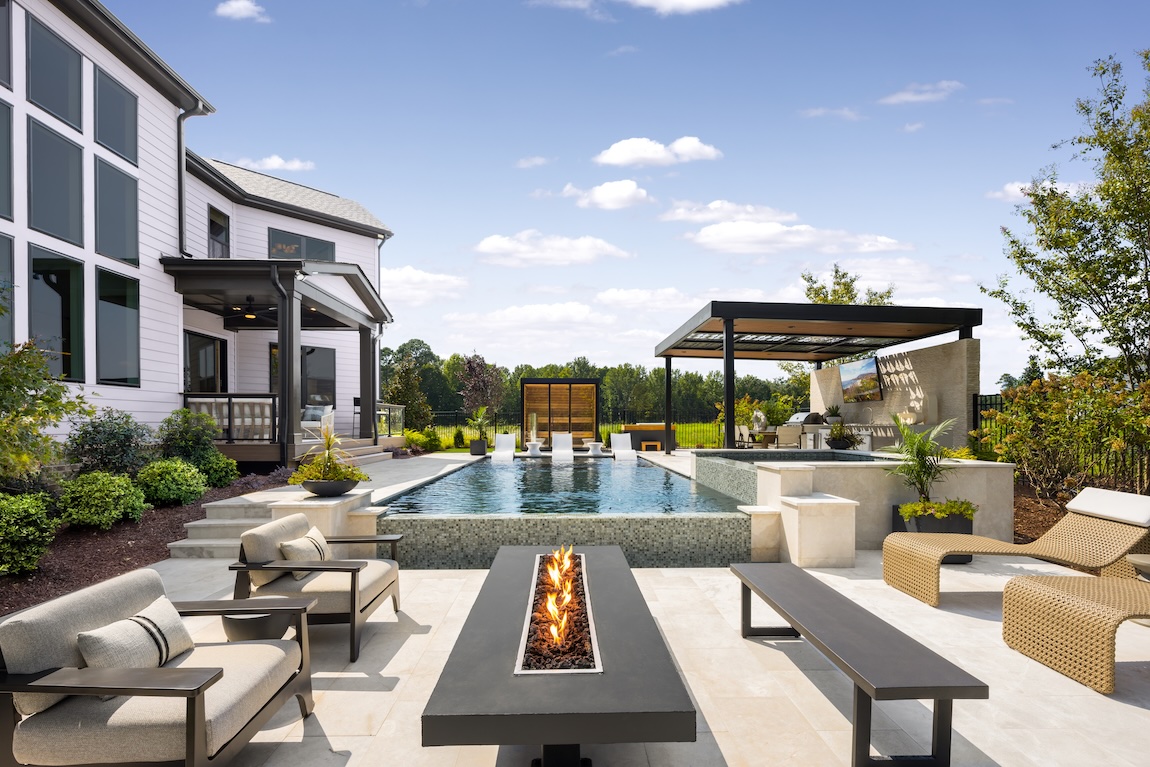 Luxury outdoor living space with a swimming pool, fire feature, lounge seating, and covered outdoor kitchen.