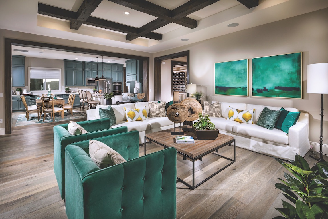 Living room with green chairs, bright kitchen cabinets and paintings.