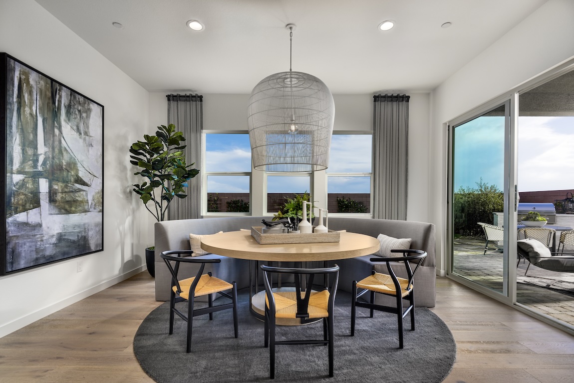 Breakfast nook with curved banquette seating, a round wood table, statement pendant lighting, and views of the outdoor living space.