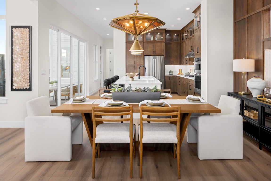 Breakfast nook with a rectangular wood dining table, upholstered seating, and statement lighting adjacent to a warm wood kitchen.