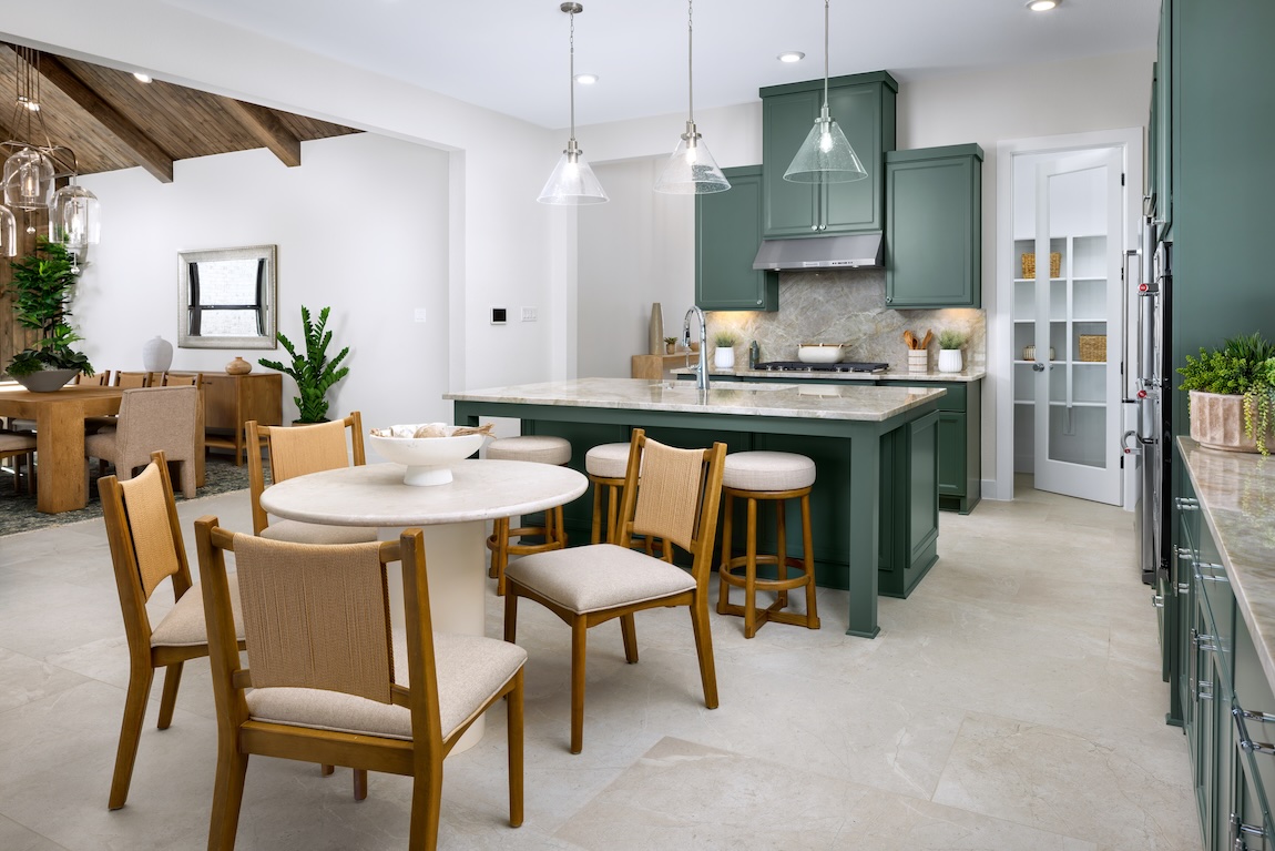 Casual dining nook with a round table and upholstered wood chairs beside a green kitchen island and cabinetry.