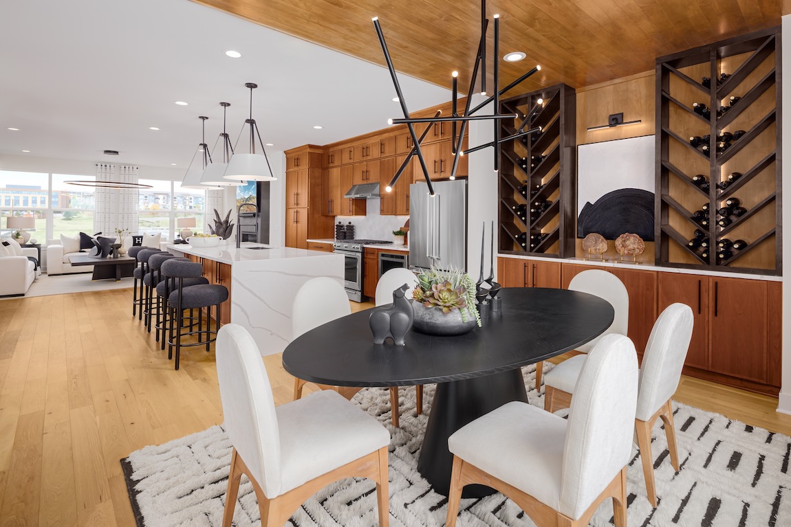 Open-concept breakfast nook with a black oval dining table, white upholstered chairs, built-in wine storage, and modern lighting.