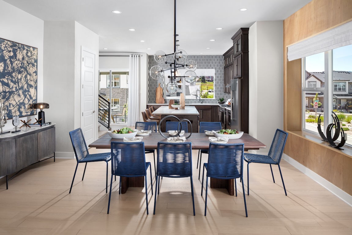 Modern casual dining area with a wood table, blue chairs, statement chandelier, and large windows overlooking the neighborhood.
