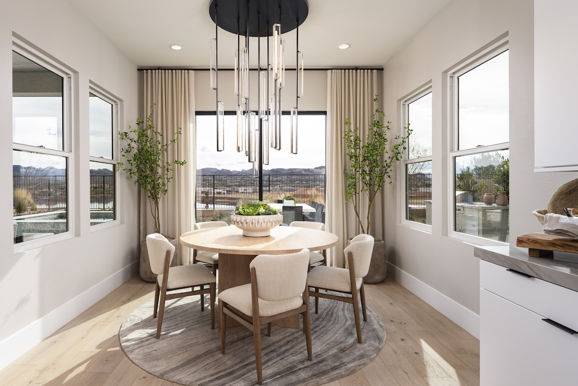 Light-filled breakfast nook with a round wood table, neutral upholstered chairs, oversized pendant lighting, and expansive windows.