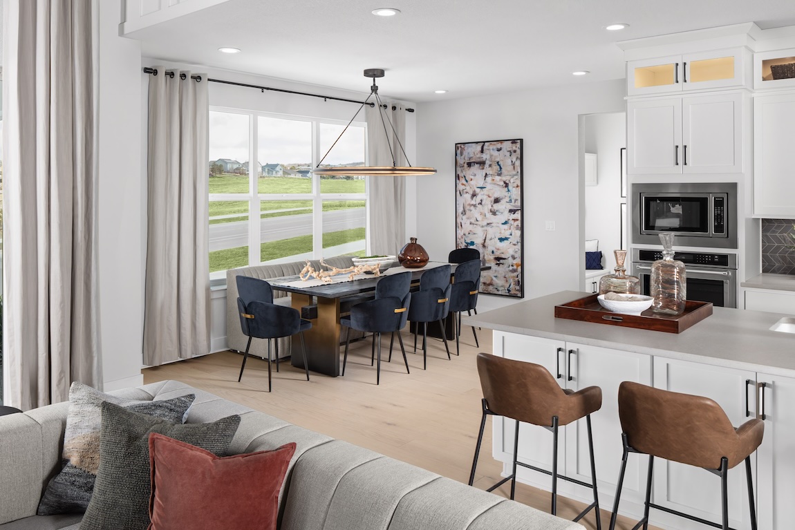 Casual dining area with a banquette, dark upholstered chairs, contemporary chandelier, and an adjacent white kitchen island.