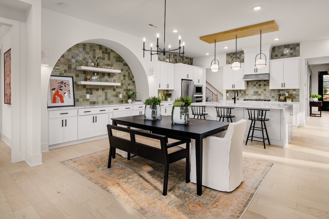 Casual dining area with a black dining table, mixed seating, and an arched built-in beside a bright white kitchen.