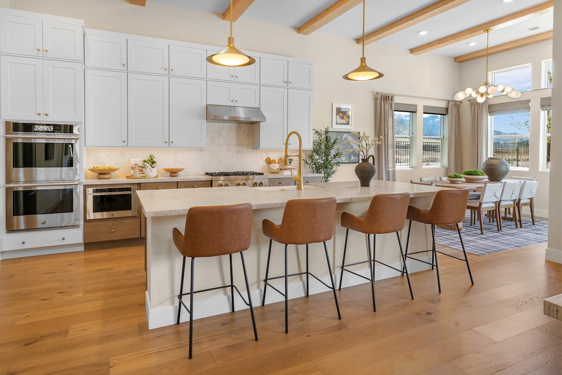 Breakfast nook with a wood dining table and upholstered chairs positioned beside a large kitchen island and expansive windows.