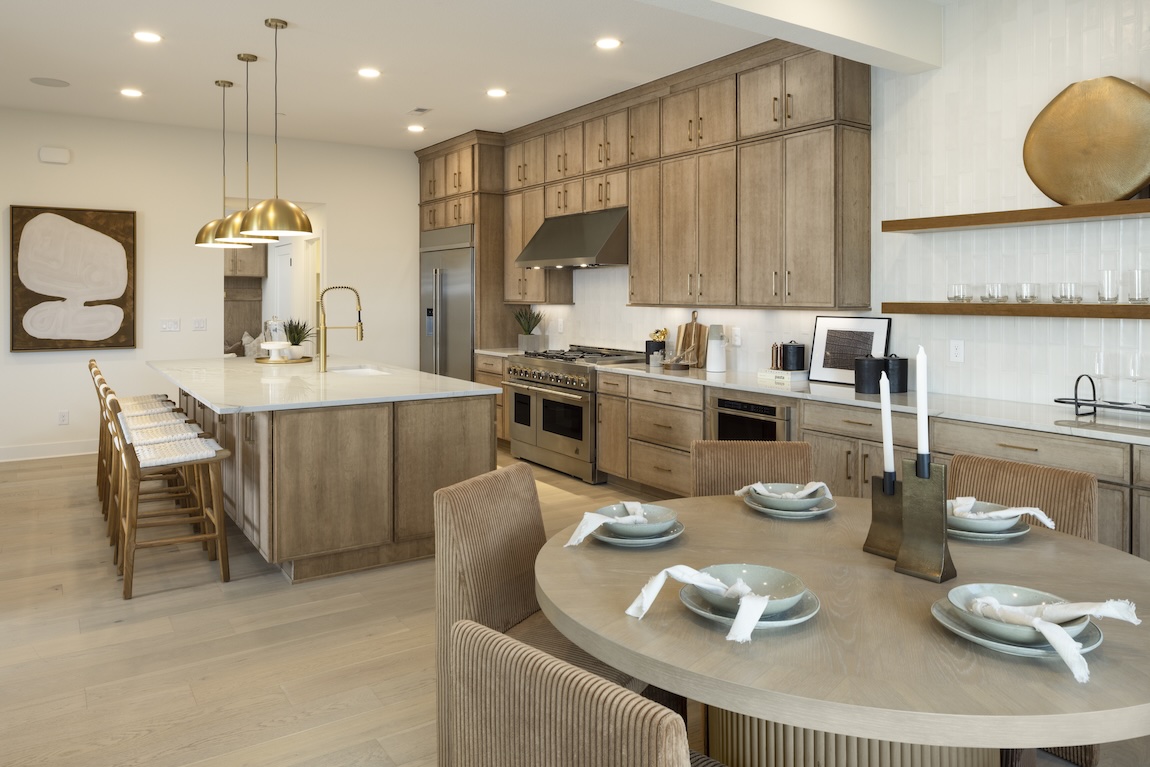 Casual dining nook with a round wood table and upholstered chairs beside a spacious kitchen with natural wood cabinetry.