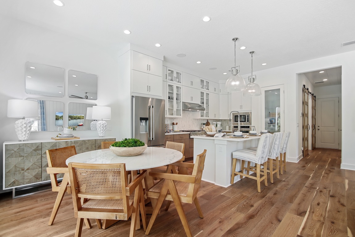 Breakfast nook with a round dining table, woven wood chairs, and an open-concept white kitchen with island seating.