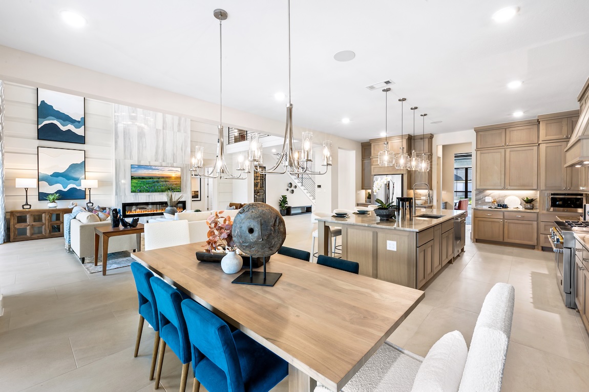 Breakfast nook with a large wood dining table, blue upholstered seating, and an open-concept kitchen and living area.