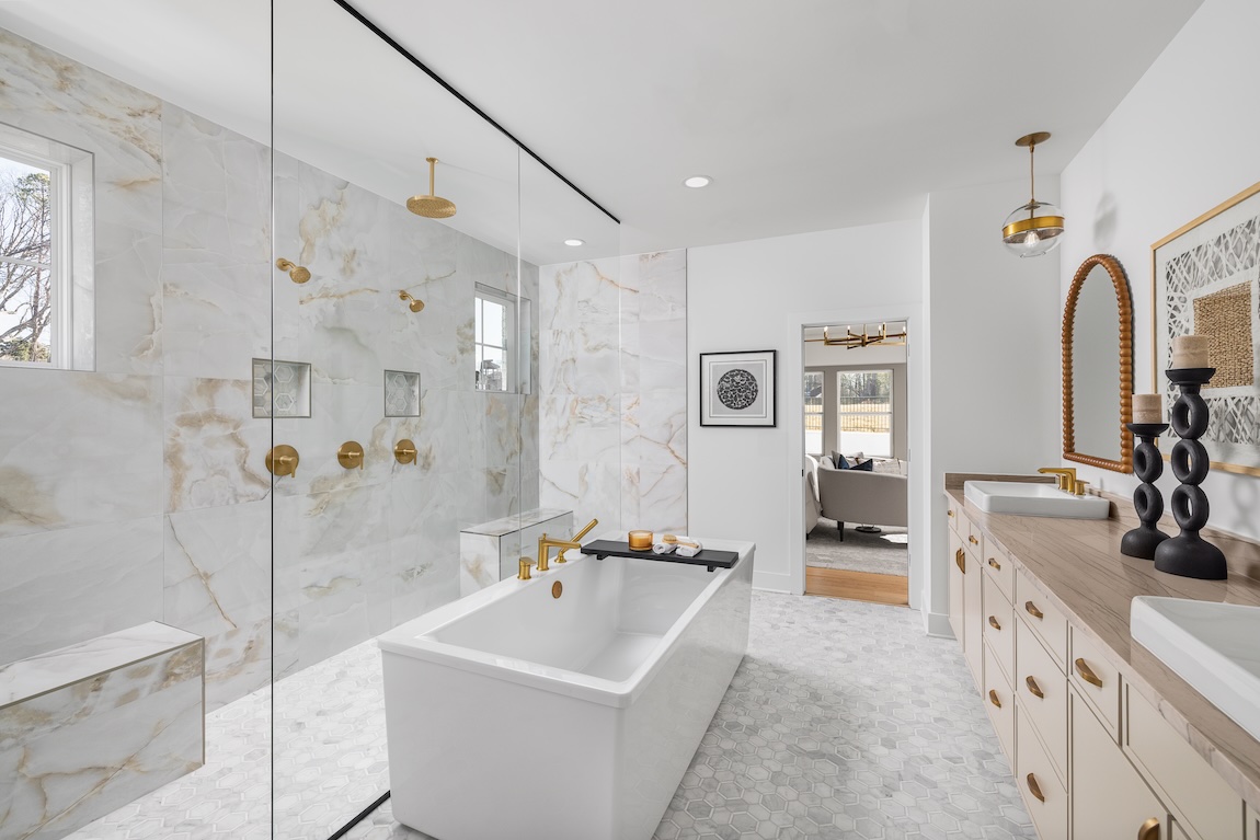 Luxury walk-in shower with marble-look tile, frameless glass, gold fixtures, built-in bench, and recessed niches.