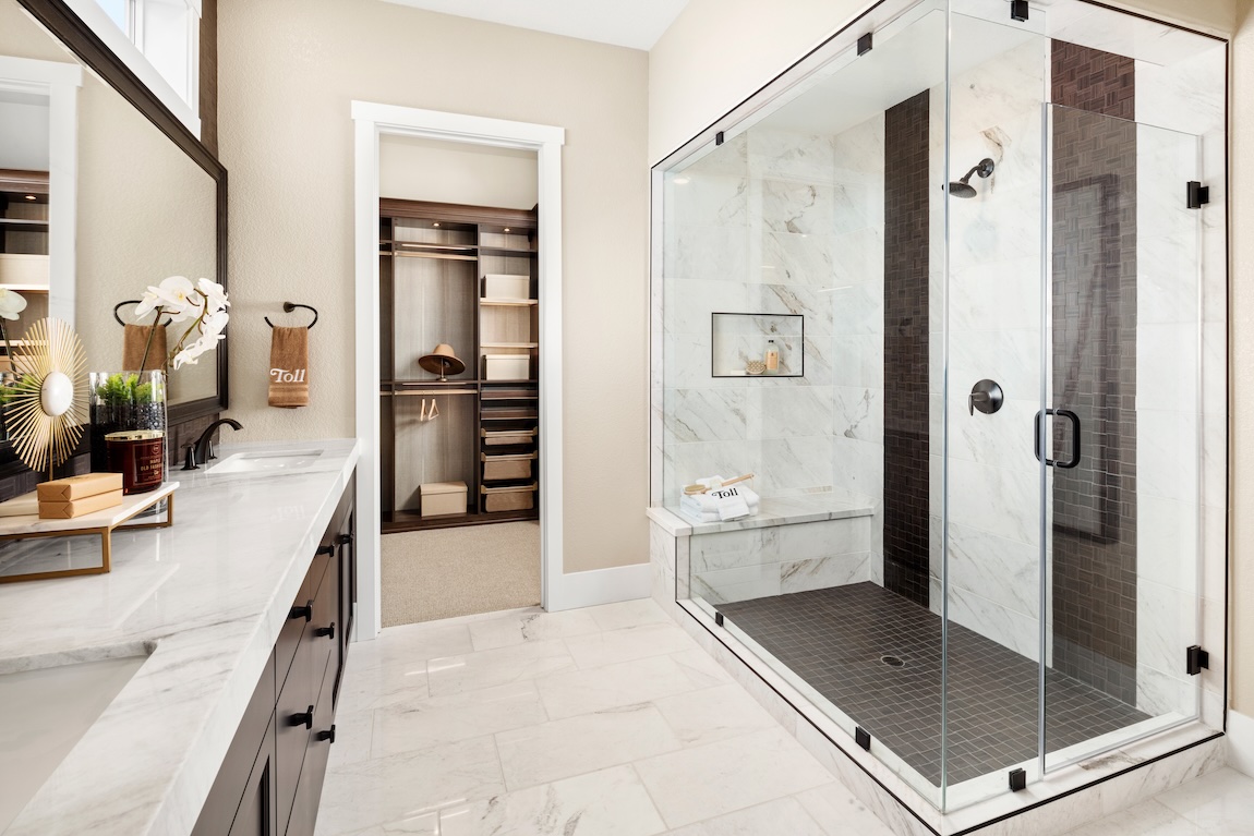 Shower with marble-look tile, contrasting dark tile accent, built-in bench, and frameless glass doors.