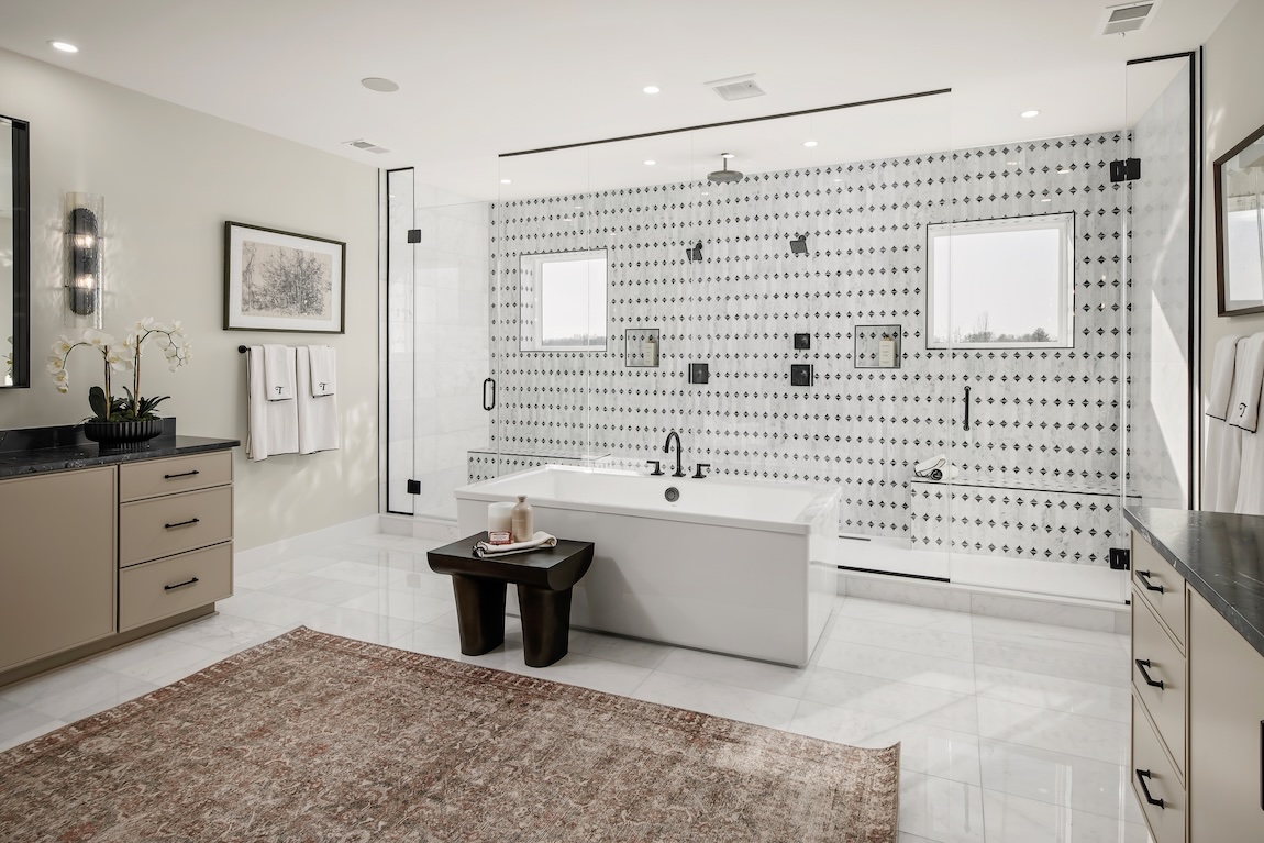 Luxury walk-in shower with a patterned tile feature wall, multiple shower fixtures, frameless glass, and adjacent soaking tub.