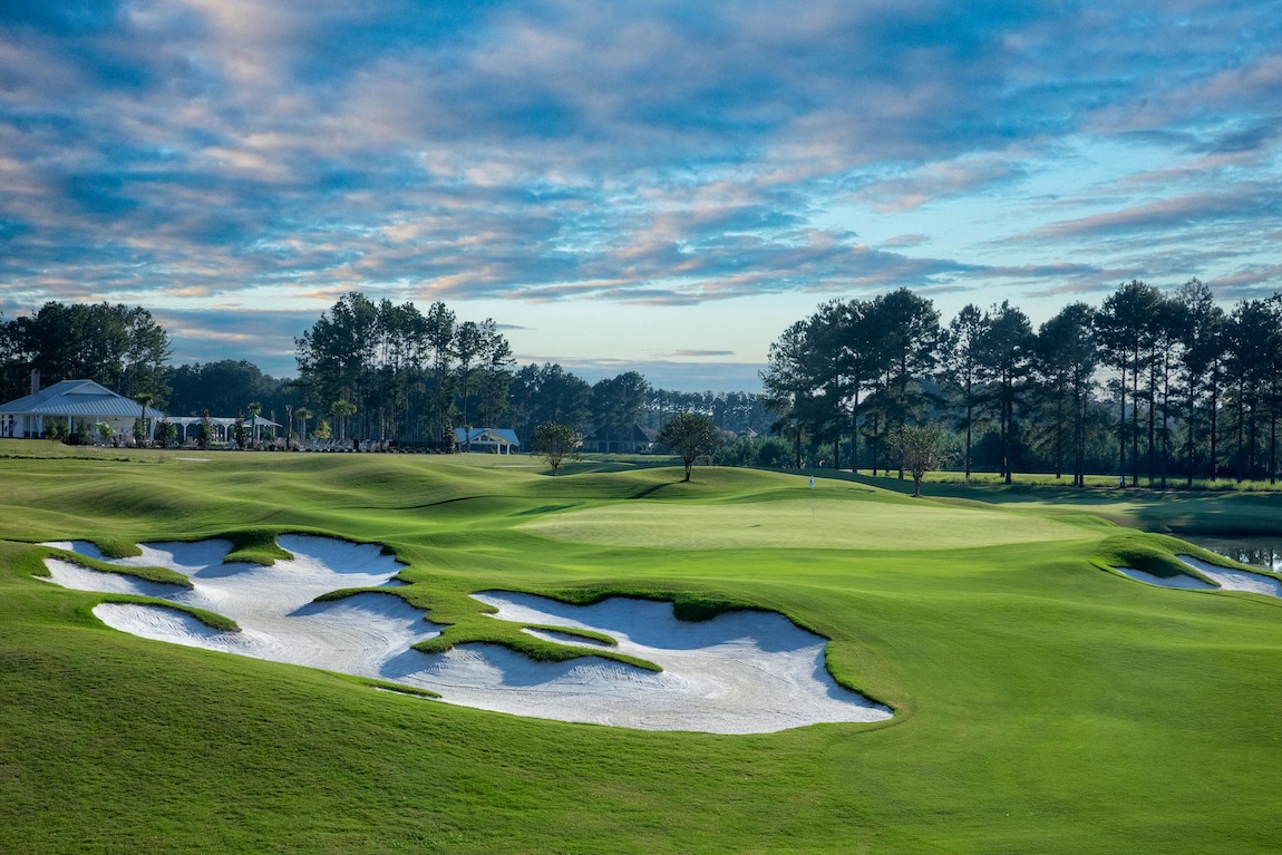 Golf course community featuring rolling fairways, sculpted sand bunkers, and lush green landscaping under a dramatic sky.
