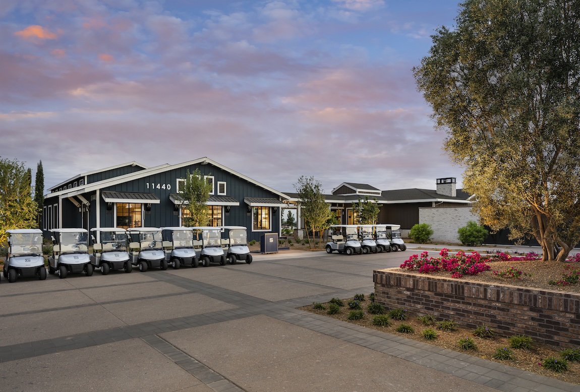 Clubhouse entrance within a golf course community featuring golf carts, landscaped grounds, and modern amenities.