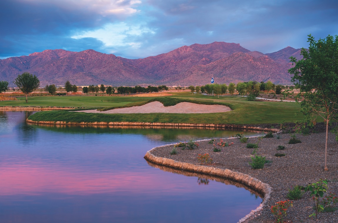 Golf course community with mountain views, lakeside fairway, and desert-inspired landscaping at sunset.