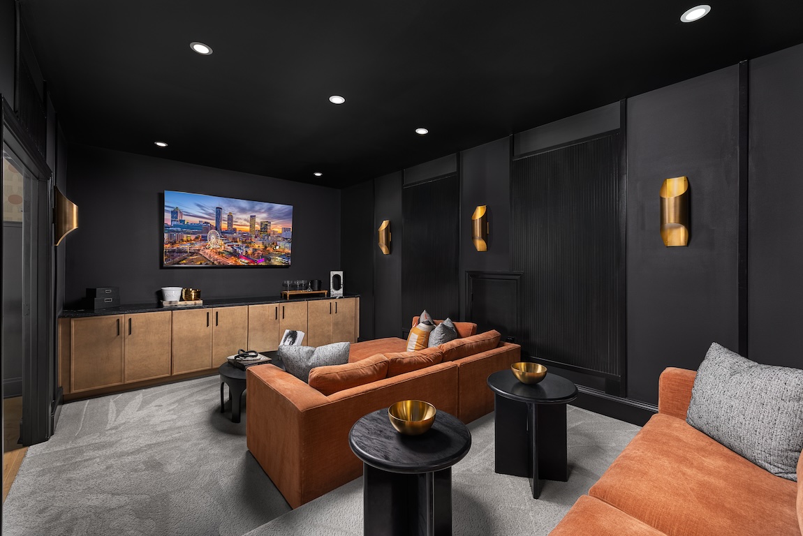 Dark home theater with black paneled walls, warm wood cabinetry, and rust-colored sectional seating.