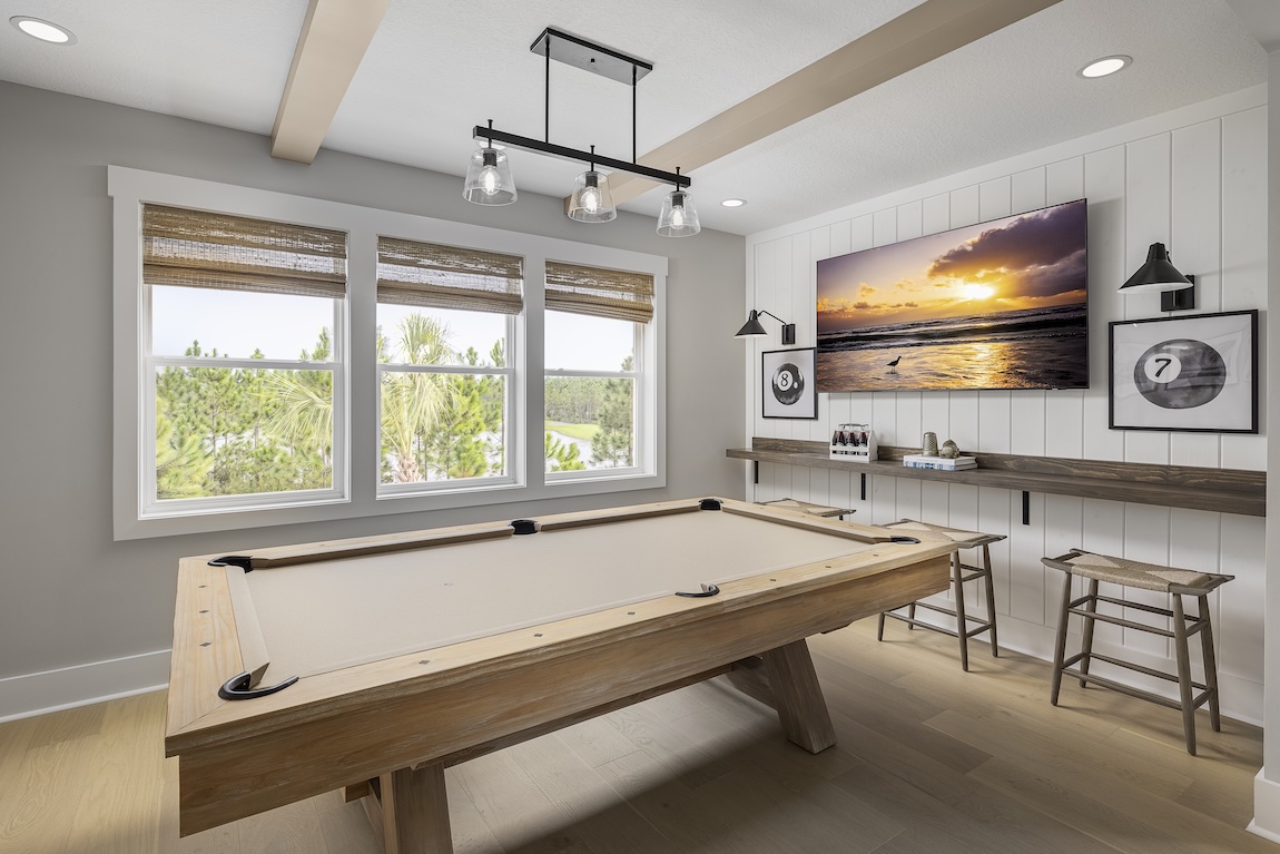 Bright game room with pool table, wall-mounted TV, bar seating, and natural wood accents.