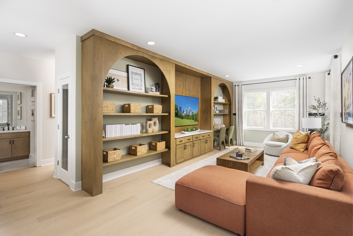 Loft living space with built-in arched shelving, media center, desk, and orange sectional sofa.