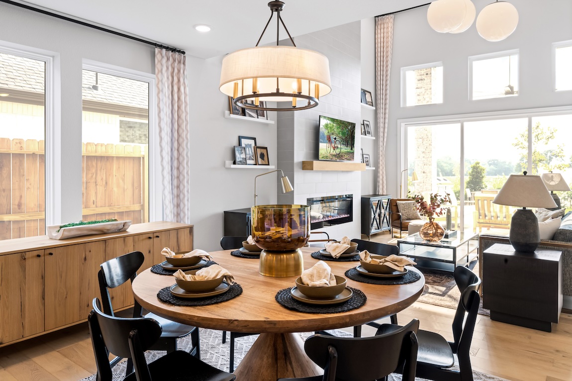Open-concept dining room with round wood table, statement chandelier, fireplace, and abundant natural light.