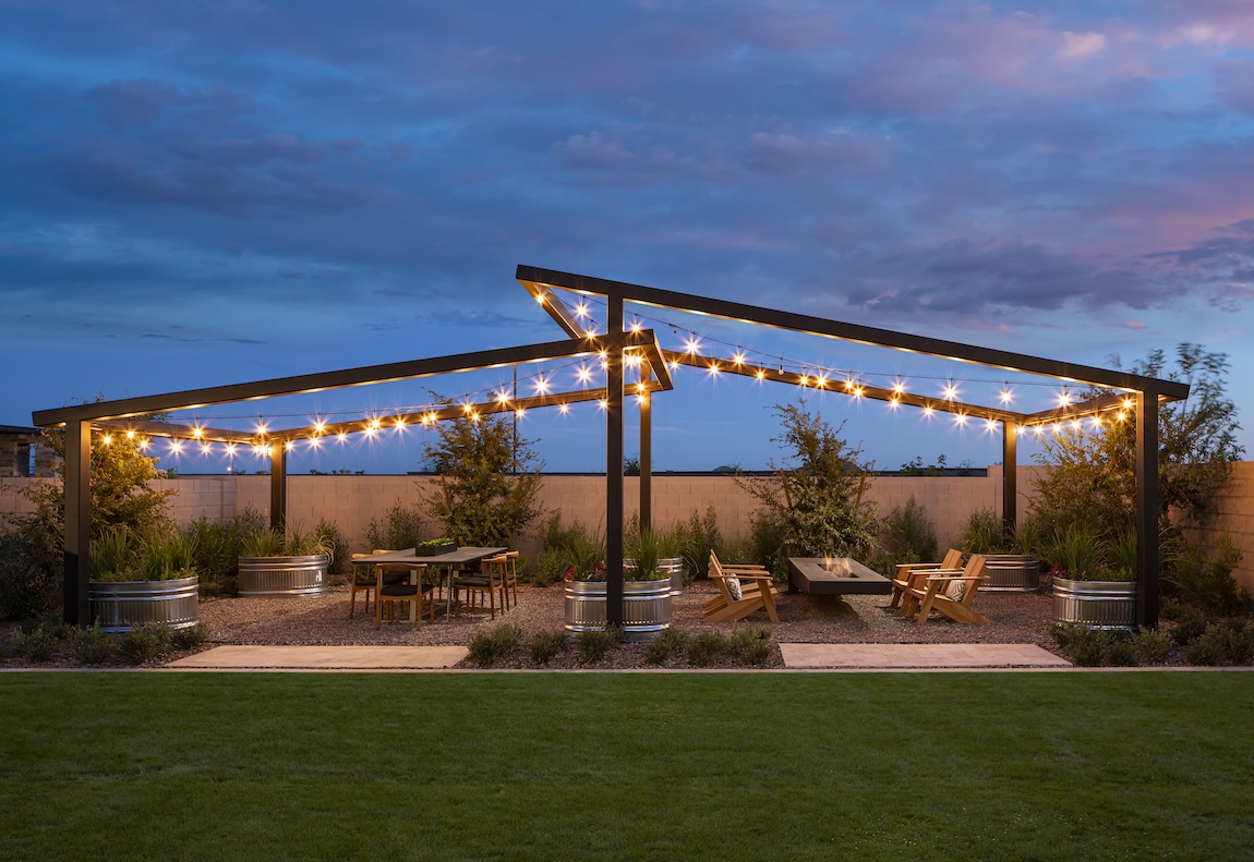 Luxury outdoor living space with fire pit, dining table, and illuminated landscaping.