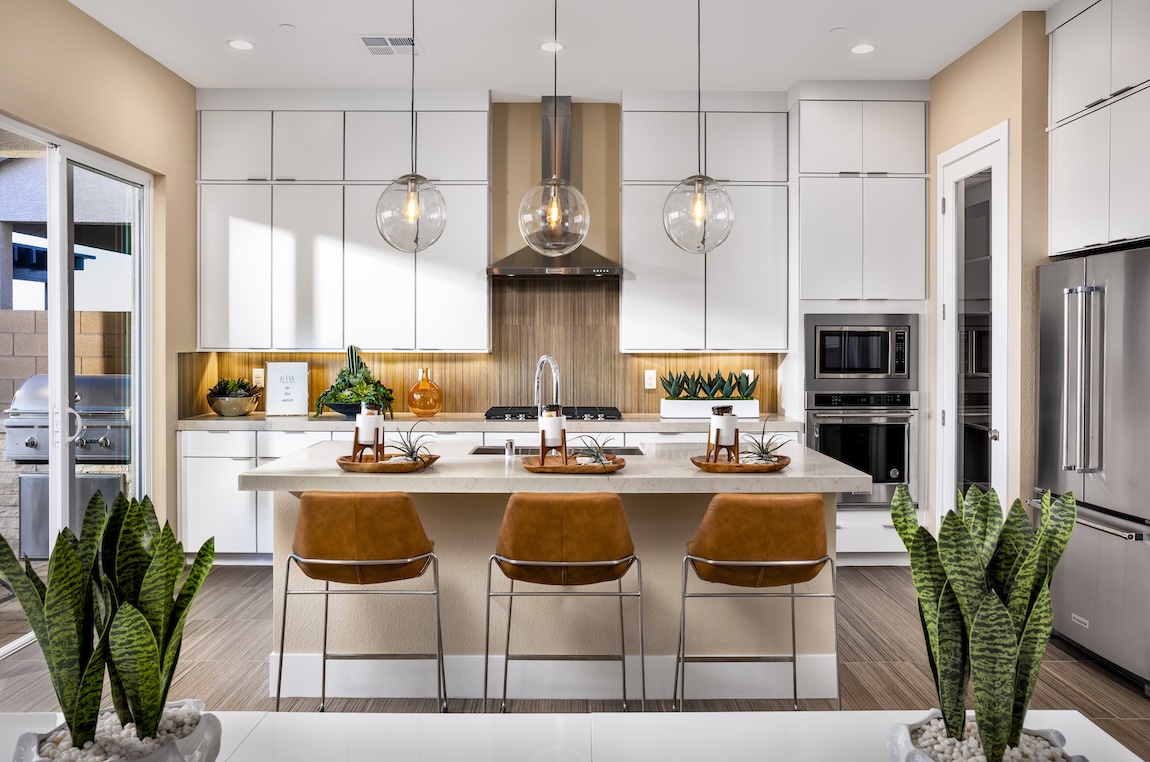 Modern white kitchen with waterfall island, leather barstools, globe pendant lights, and warm wood accents.