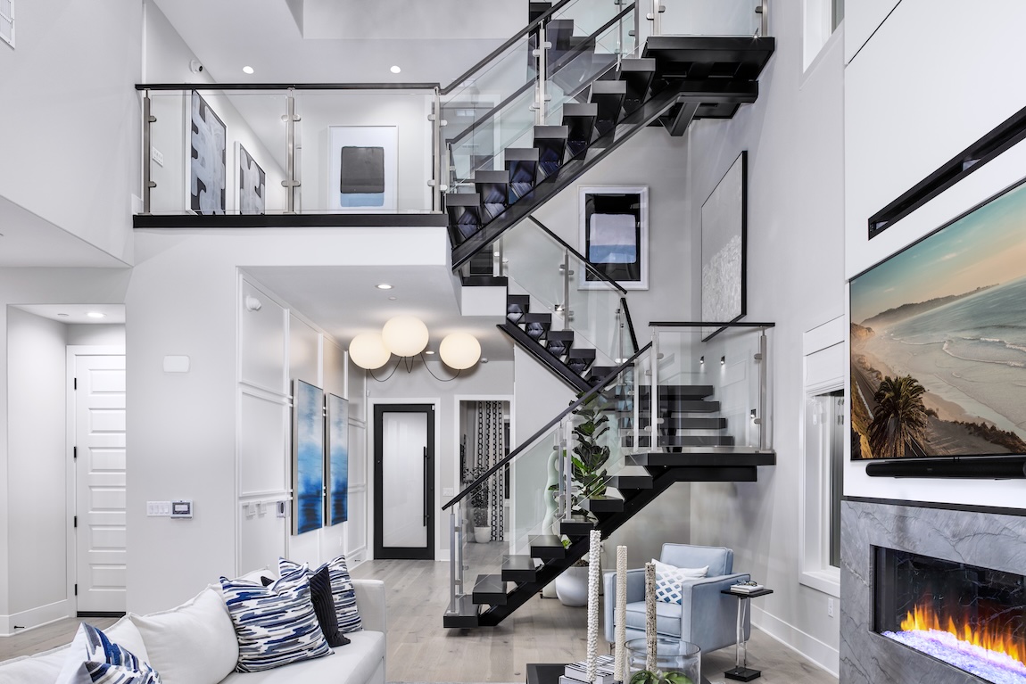 Contemporary staircase with glass panels and black floating treads in a coastal-inspired living room with modern decor and fireplace
