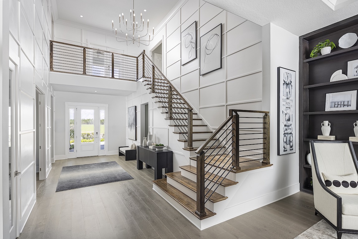 Modern staircase with dark wood treads and horizontal railings in a bright two-story foyer featuring grid panel walls, minimalist artwork, and open shelving