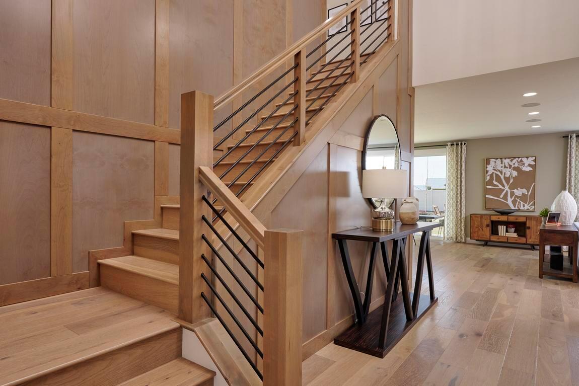 Warm wood staircase with horizontal metal railings in a double-height foyer featuring paneled accent walls, modern chandelier, and open-concept layout