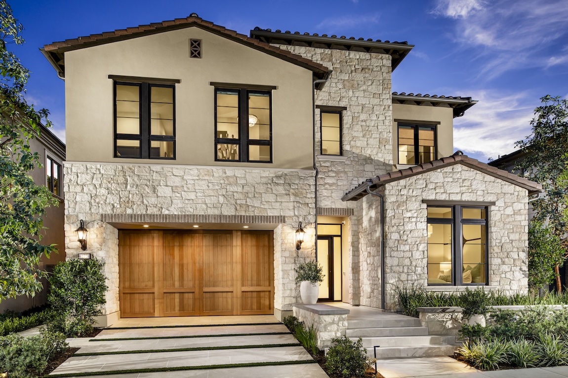 exterior of stone home with greenery and warm interior lighting.