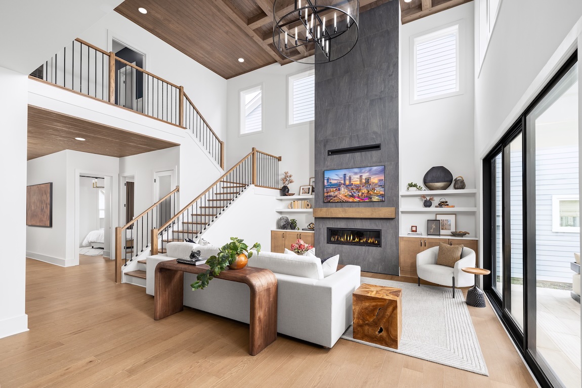 Two-story great room with a floor-to-ceiling fireplace, wood ceiling details, open staircase, and expansive windows.
