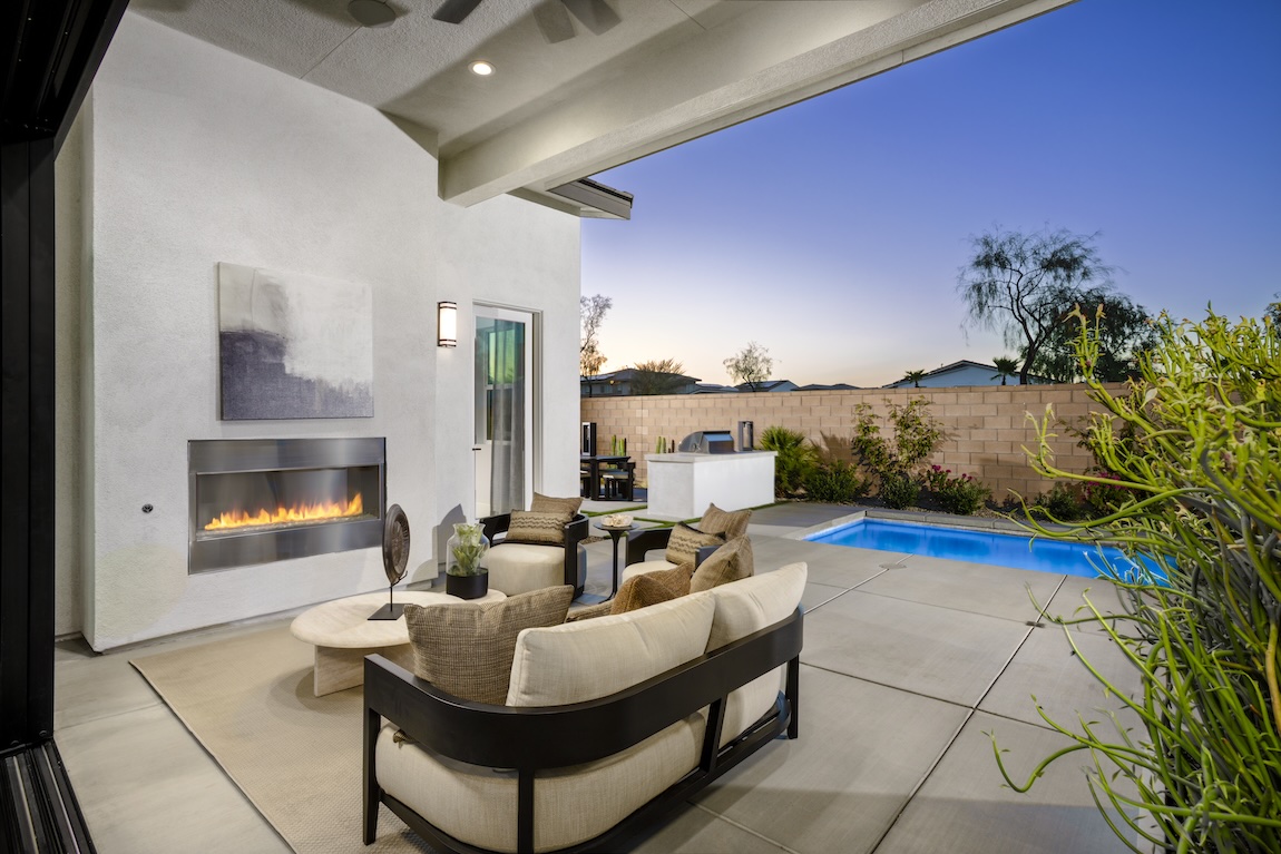 Covered patio with modern fireplace and lounge seating beside a private pool.