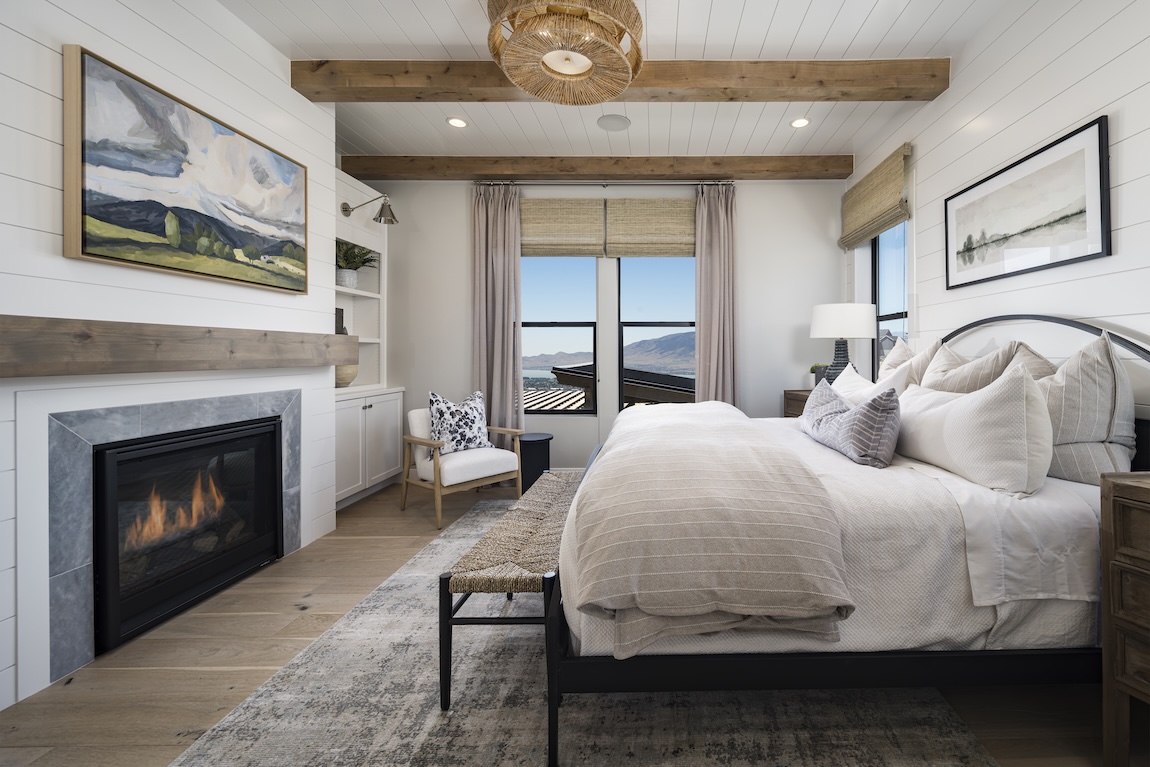 Serene bedroom with mountain views and a modern fireplace beneath rustic wood beams.