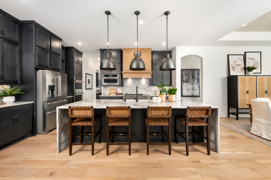 Kitchen design with white quartz waterfall countertops and black cabinets with rattan high chairs on the island.