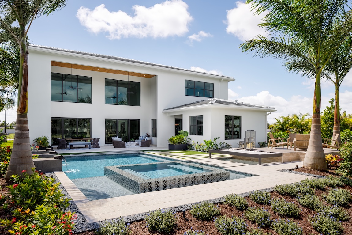 Backyard pool with greenery surrounding and views of the exterior of a modern home.
