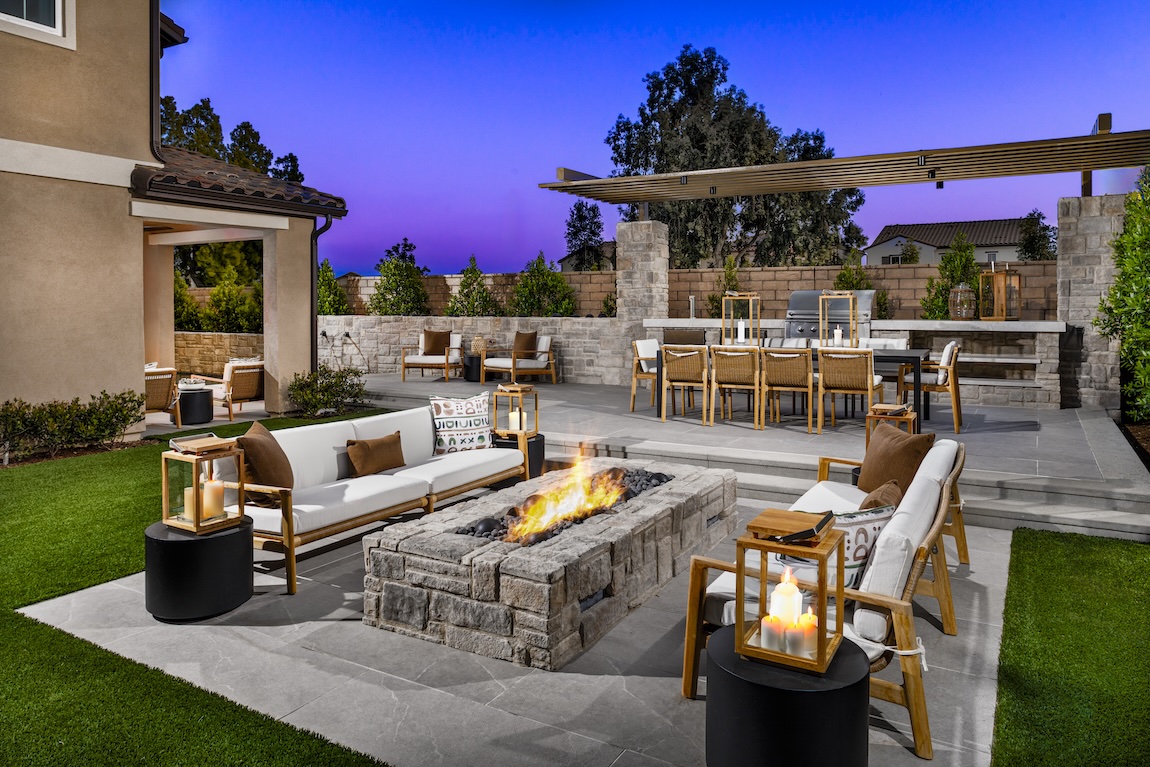 Backyard patio featuring a modern fire pit, outdoor lounge seating, and a built-in kitchen with dining area, blending luxury design with functional barbecue space.