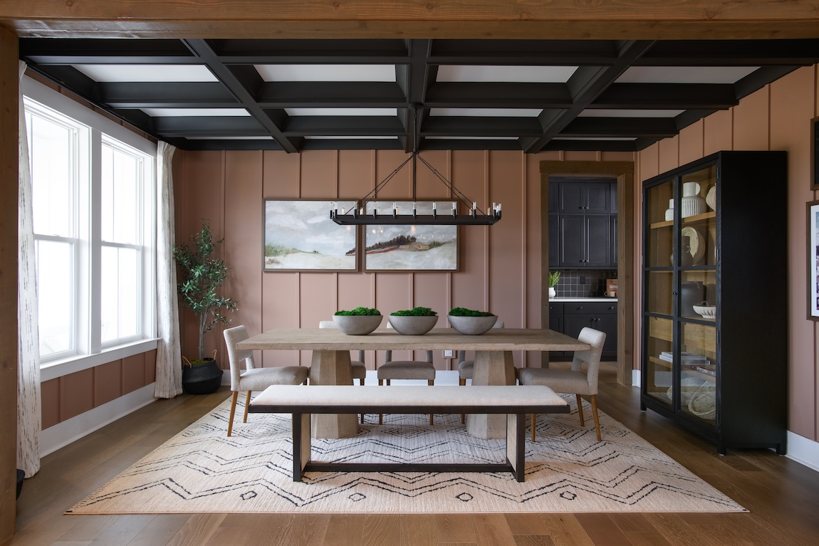 Sophisticated farmhouse dining room with terra-cotta vertical paneling, black beamed ceiling, and rustic wood furniture accented by neutral upholstered chairs and a geometric rug.