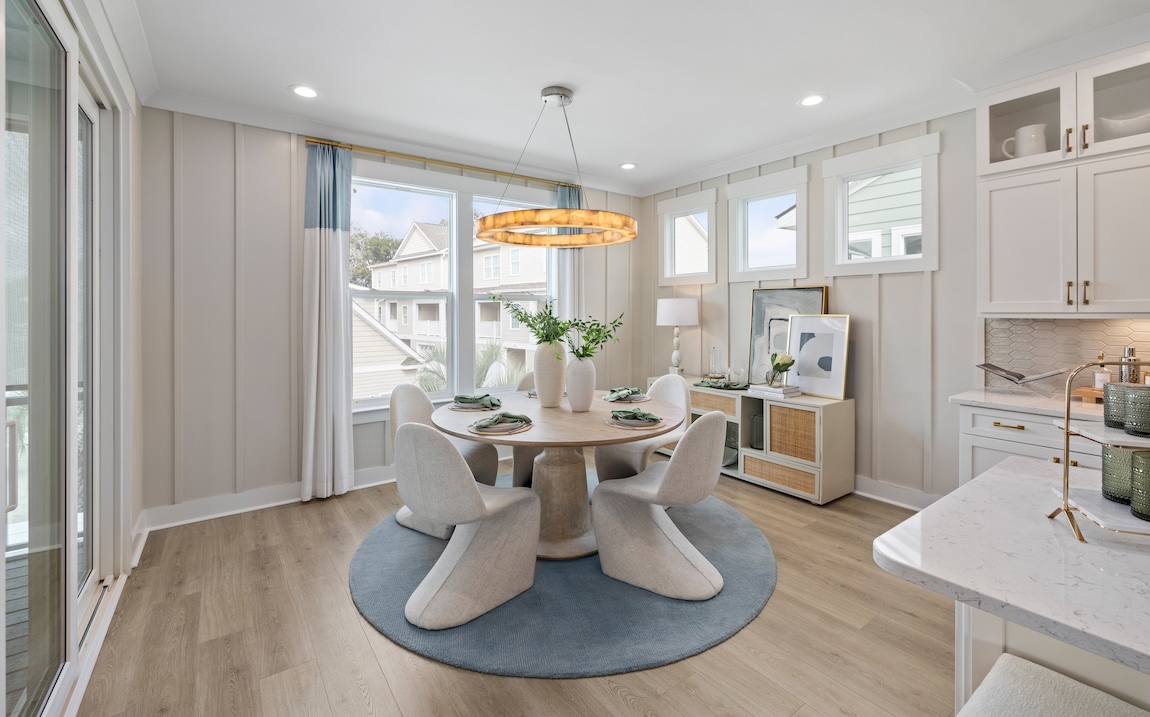 Light-filled breakfast nook with pale oak floors, soft cream and blue tones, circular modern table and curved dining chairs, styled for airy coastal elegance in a Toll Brothers home.