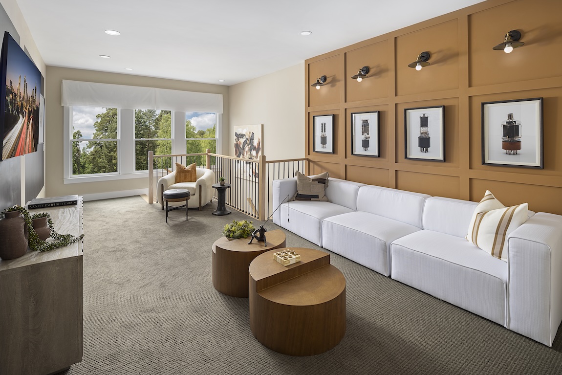 Warm-toned loft with Bosc pear accent wall paneling from the Sherwin-Williams 2025 color capsule, white sectional sofa, and dual round wood coffee tables, blending mid-century and transitional styles in a cozy upstairs retreat.