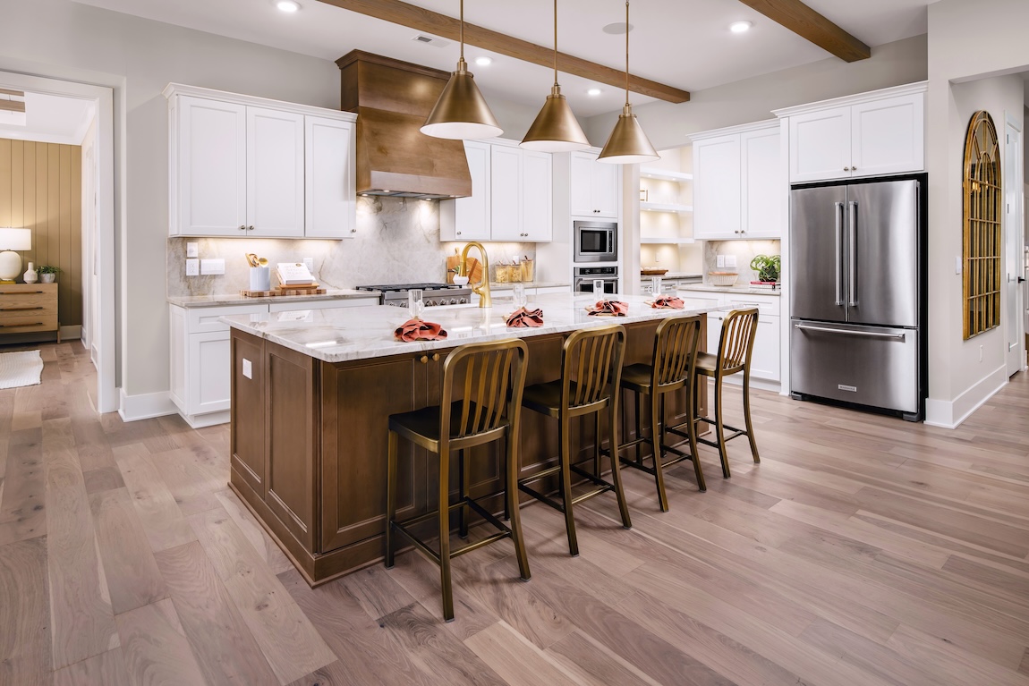 Elegant kitchen with warm wood island, white shaker cabinets, gold pendant lighting, and marble countertops. Light oak floors and stainless steel appliances complete this refined, contemporary Toll Brothers design.