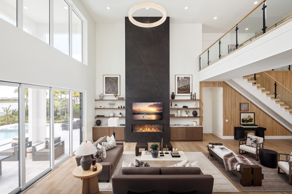 Two-story great room with a floor-to-ceiling fireplace, floating wood shelves, expansive windows, and open staircase.