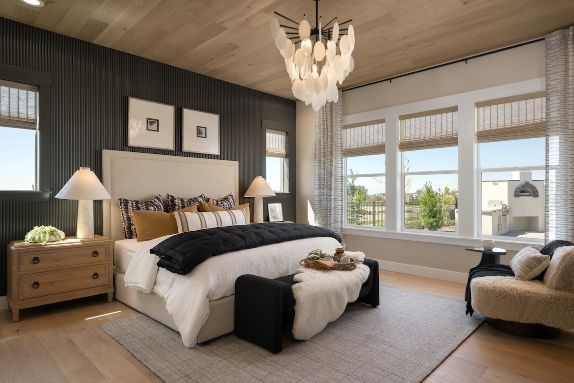 Modern primary bedroom with a wood-paneled ceiling, fluted accent wall, statement chandelier, and layered neutral furnishings.