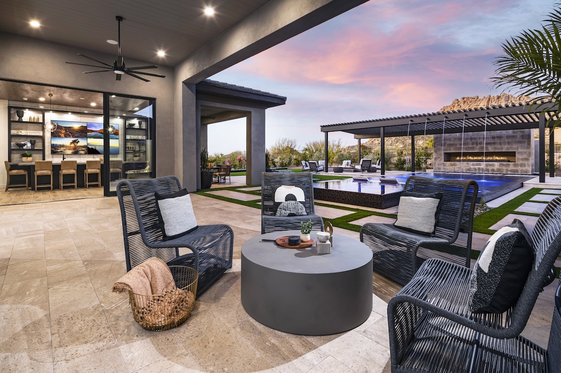 Modern outdoor living space with lounge seating, pool, and fireplace against a desert sunset backdrop.