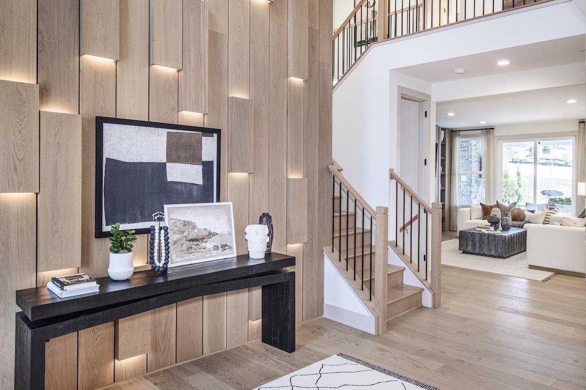 Modern foyer with wood-accent wall, sleek console table, and open staircase leading to a bright living space.