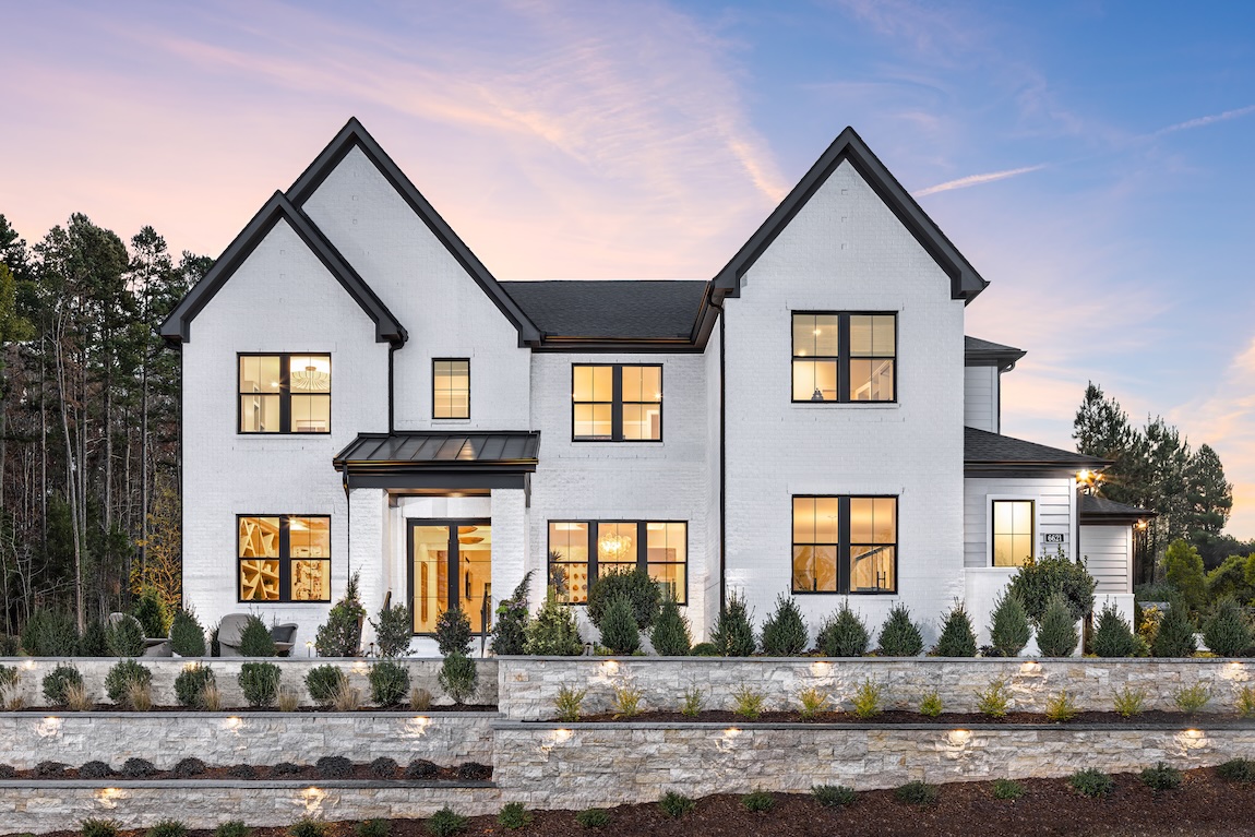 Modern white brick home with black trim and tiered landscaping at dusk