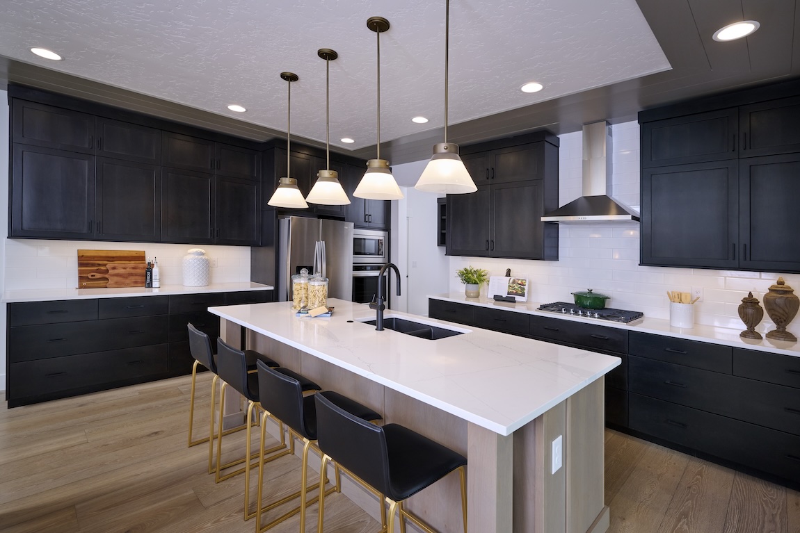 Contemporary kitchen featuring matte black cabinets, a white quartz island with seating, brass-accented bar stools, subway tile backsplash, and minimalist pendant lighting.