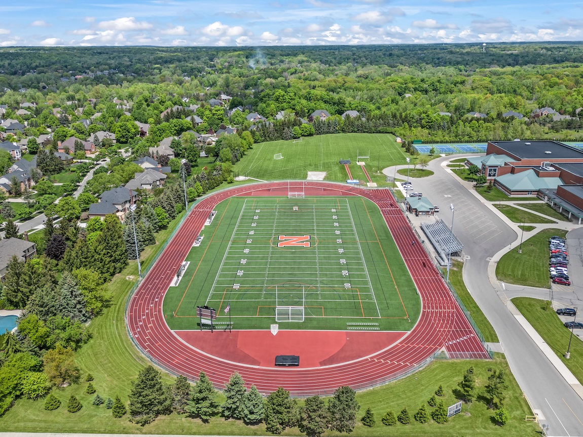 Aerial view of a Northville high school athletic complex with a football field, running track, tennis courts, and surrounding residential neighborhood.