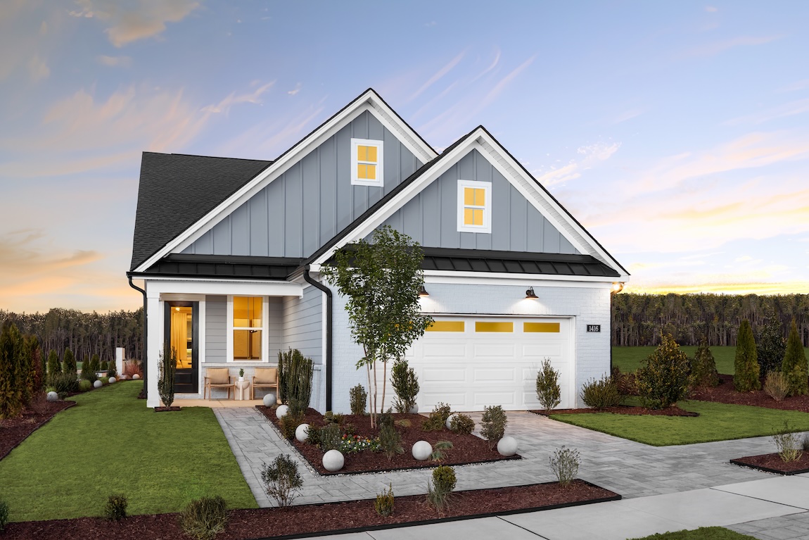 Modern farmhouse-style home with light gray siding, white brick accents, black metal roof details, and landscaped front yard at sunset.