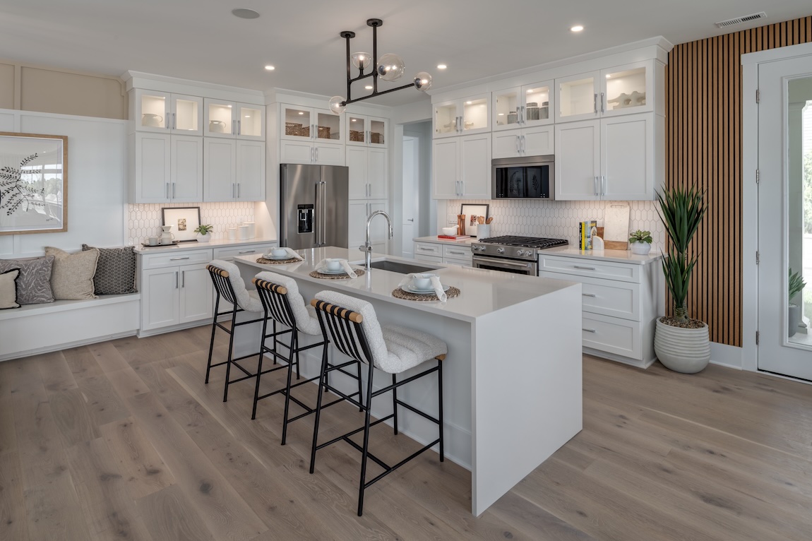 Bright modern kitchen with white cabinetry, a large white island with seating, glass-front upper cabinets, stainless steel appliances, and light wood flooring in Northville, Michigan